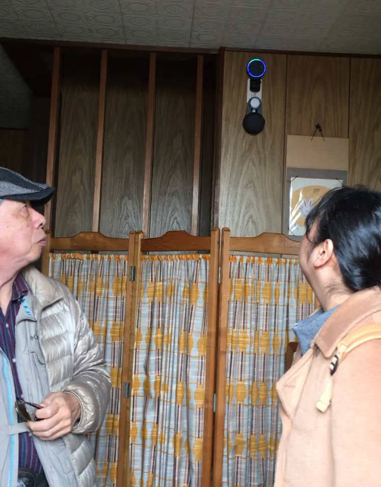 玄関でアレクサを見上げる園さんと丸井さんの写真